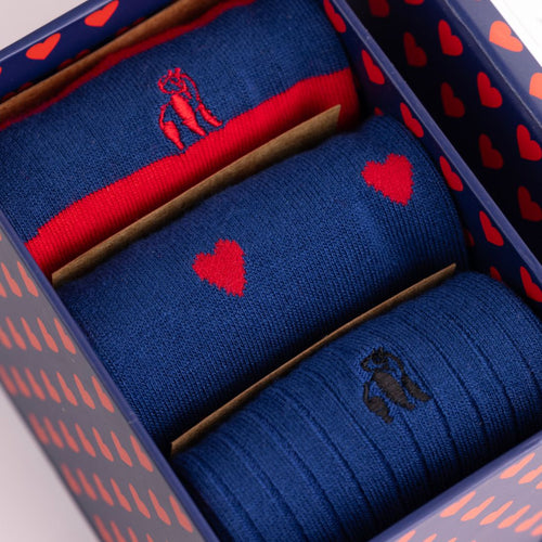 Three pairs of blue and red socks in a decorative box with heart patterns.
