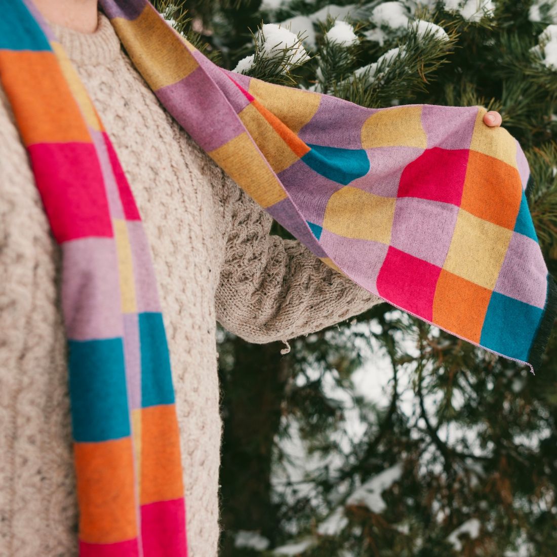 Colorful checkered scarf held by a person against a snowy background