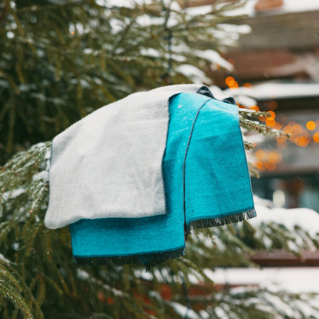 Stack of blue and gray fabric on a snow-covered branch with blurred lights in the background