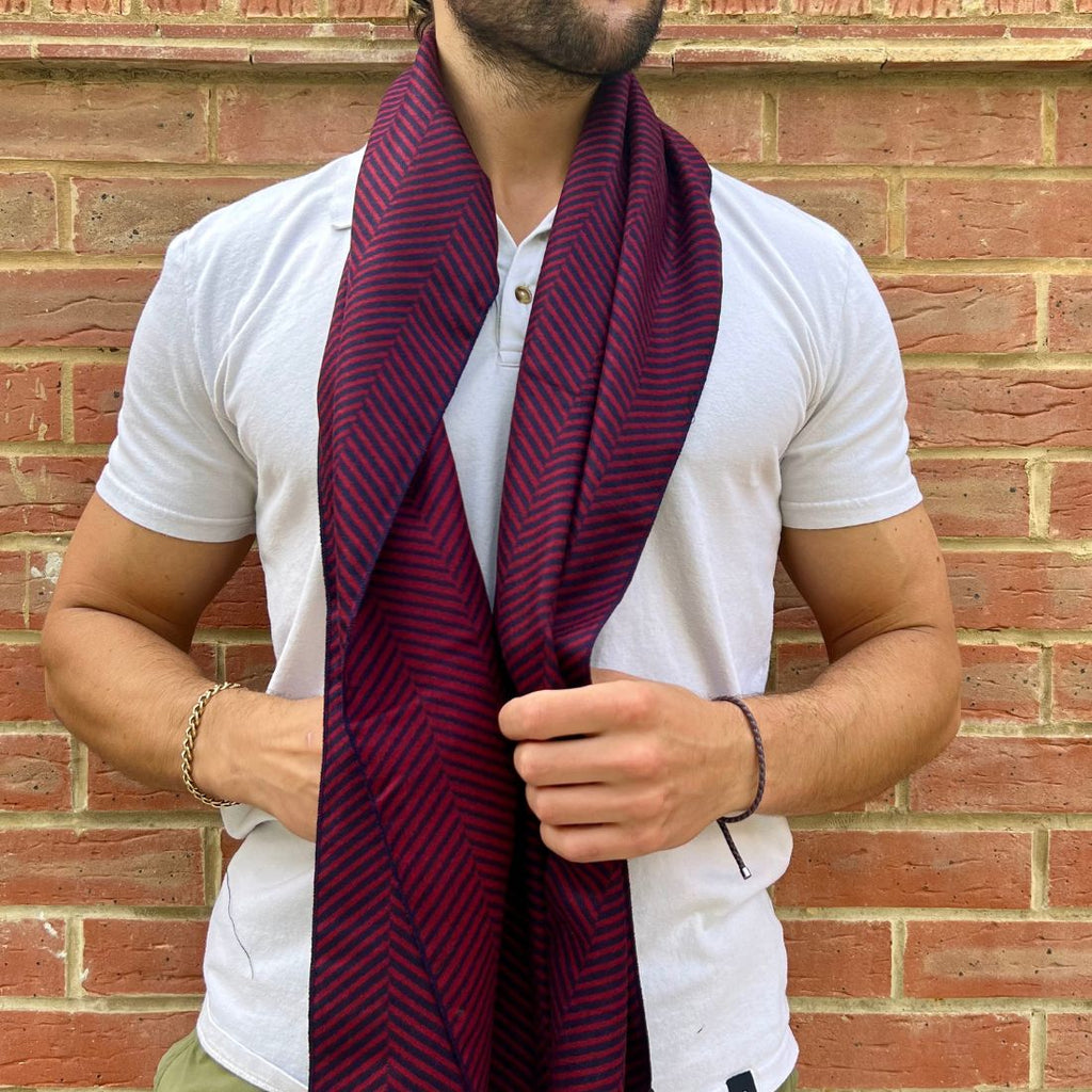 Man wearing a white shirt and a red and black striped scarf against a brick wall.