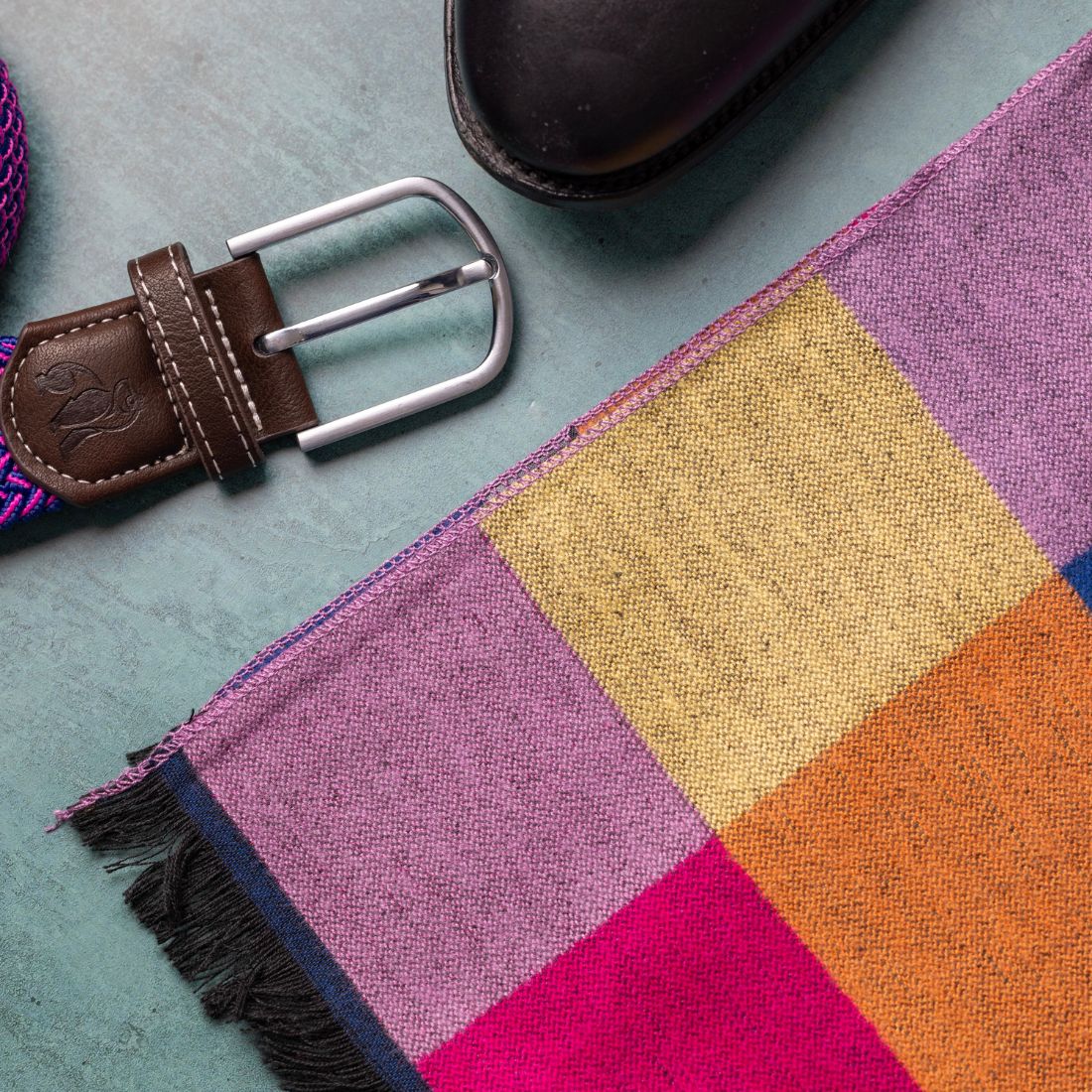 Colorful checkered scarf with a brown belt on a textured surface