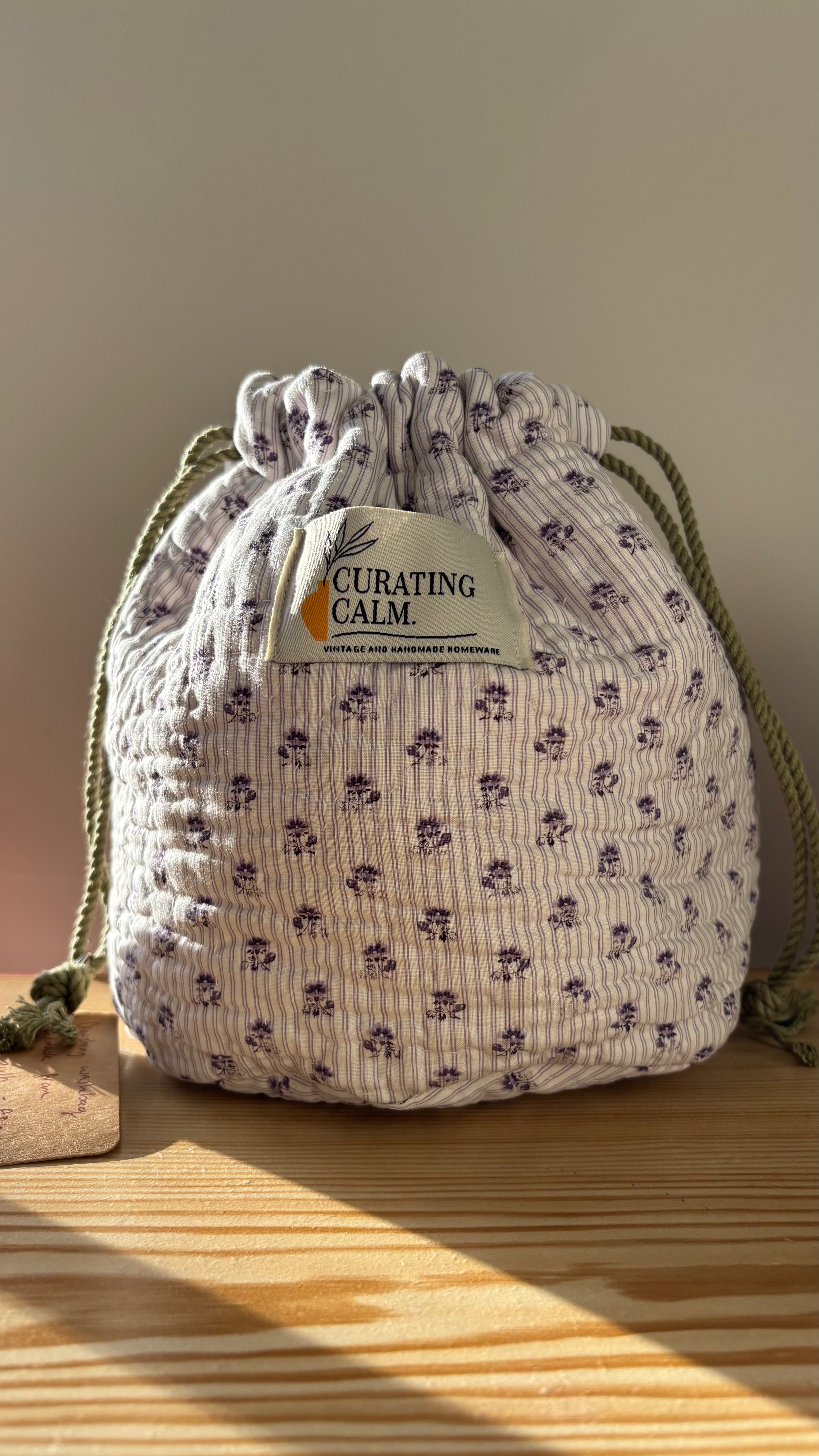 Drawstring bag with 'Curating Calm' label on a wooden surface