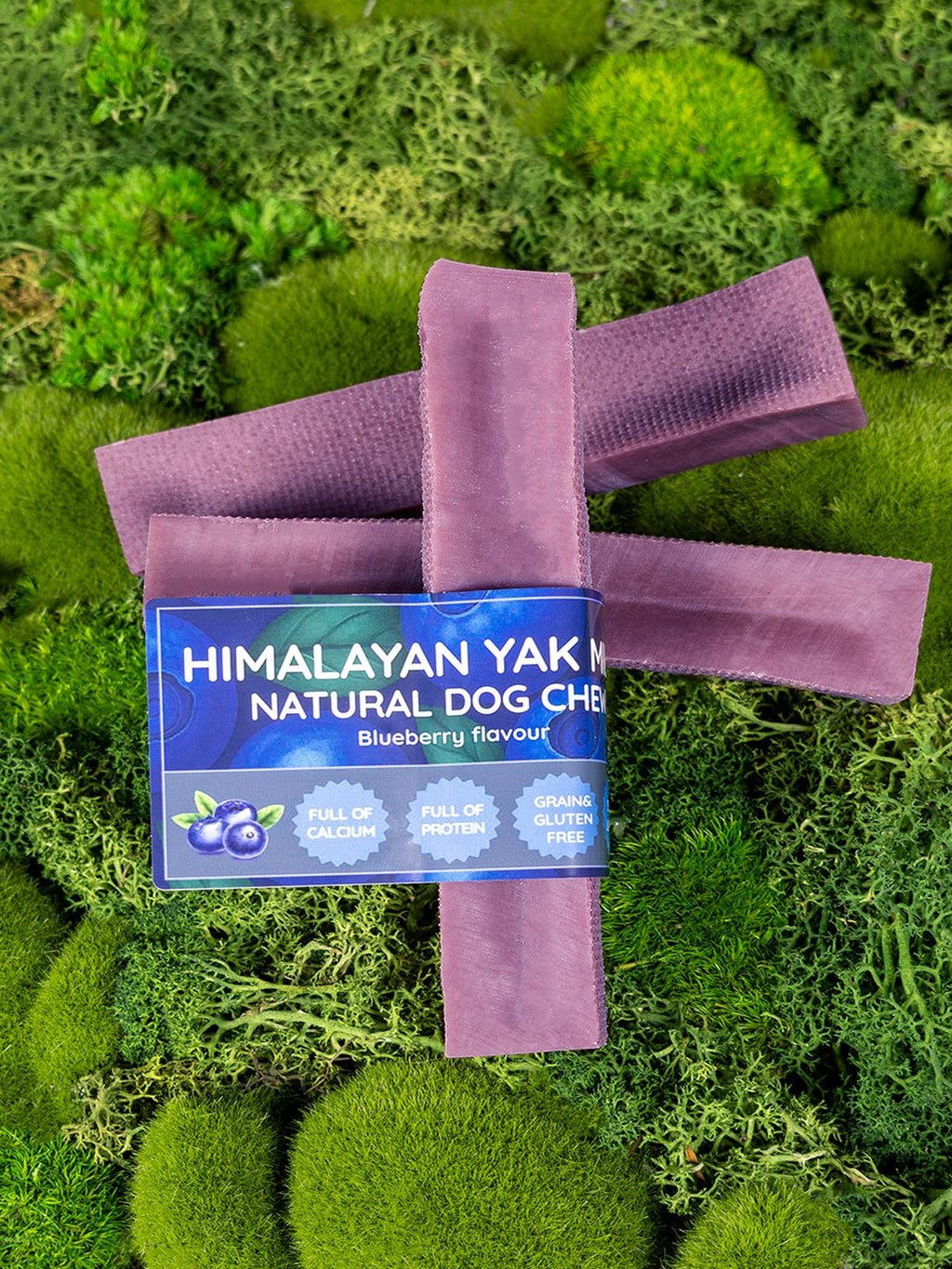 Purple dog chew with Himalayan Yak Natural Dog Chew packaging on a green moss background