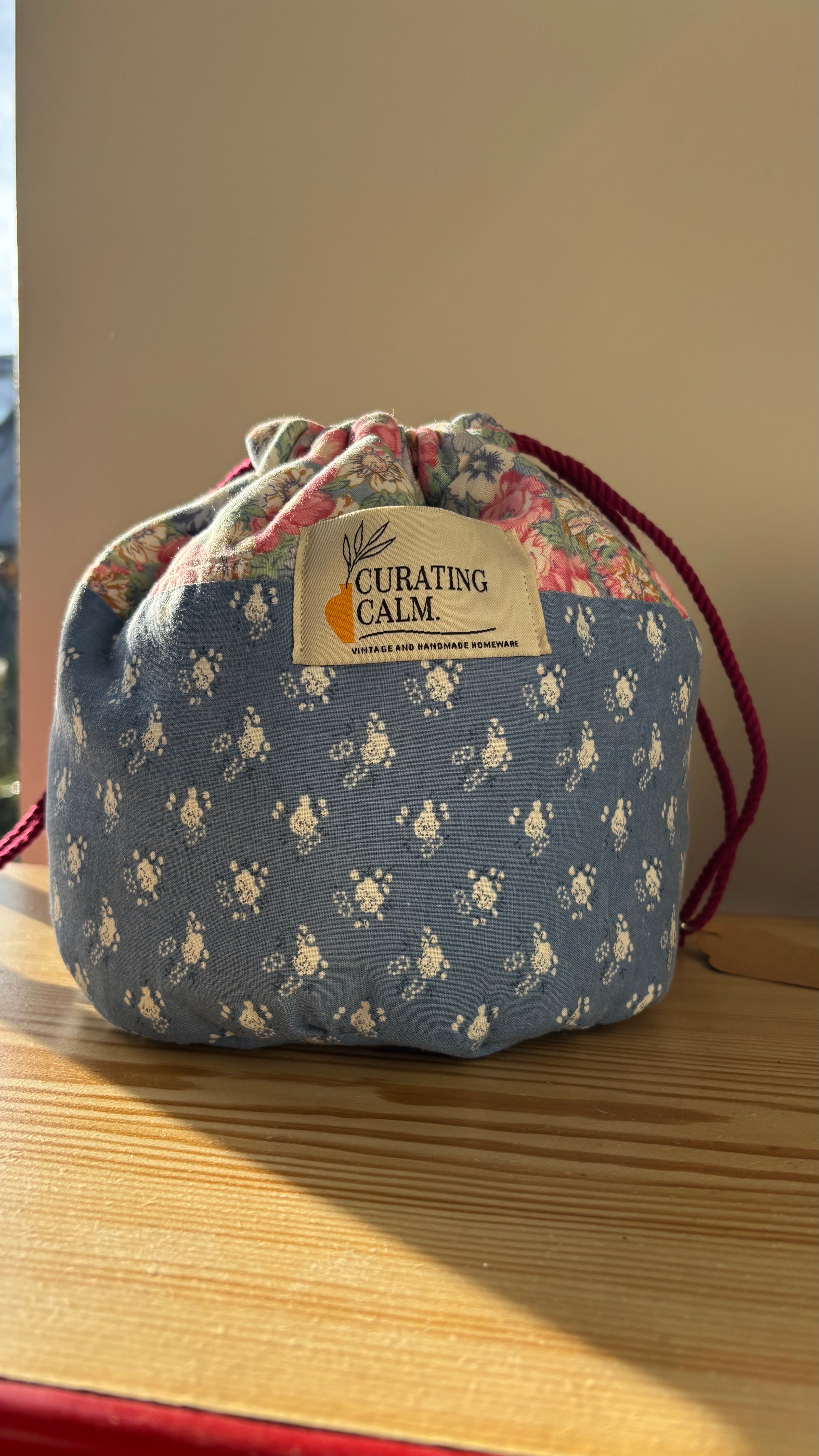 Floral drawstring bag with 'Curating Calm' label on a wooden surface