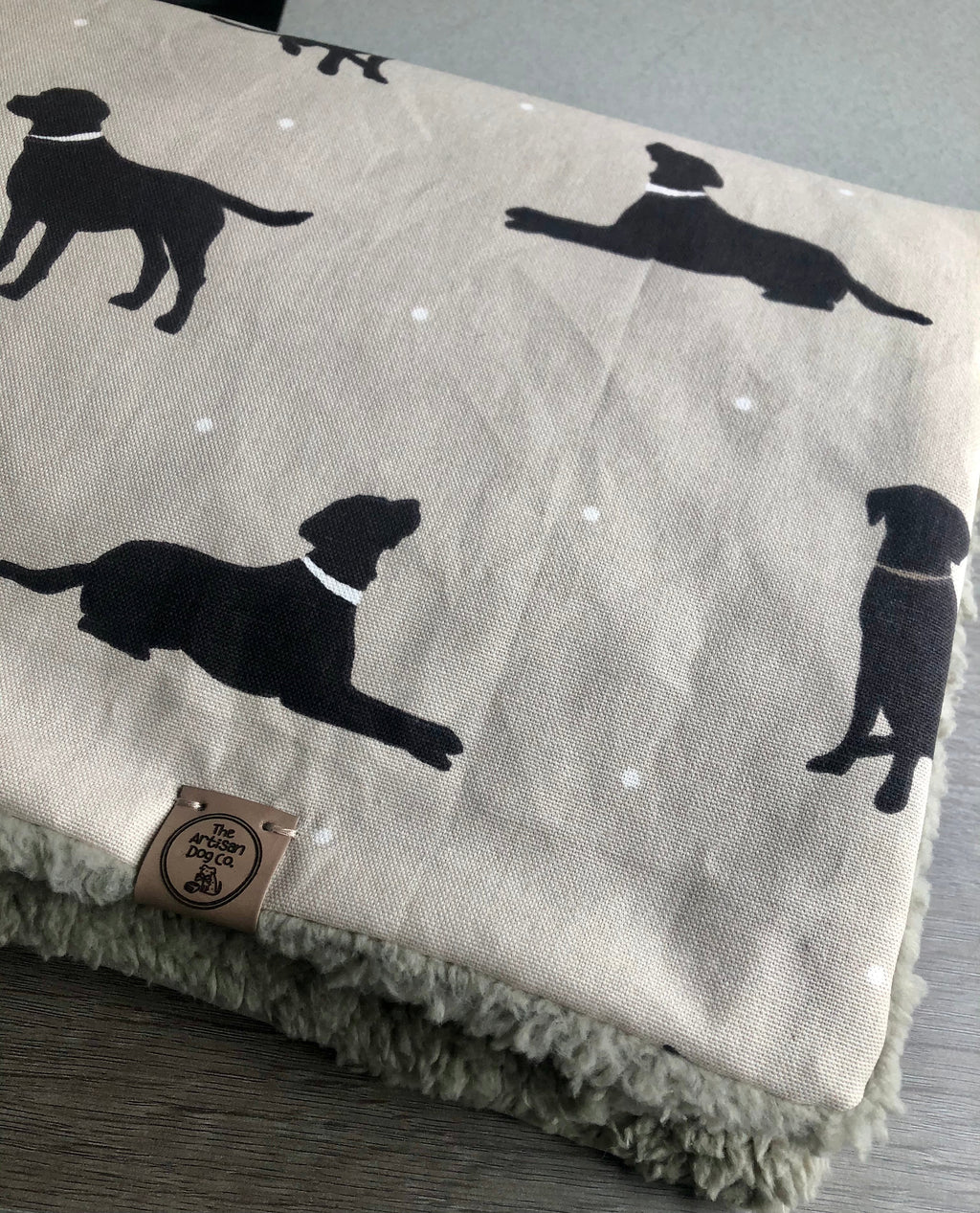Gray blanket with black dog silhouettes and a brand label on a wooden surface