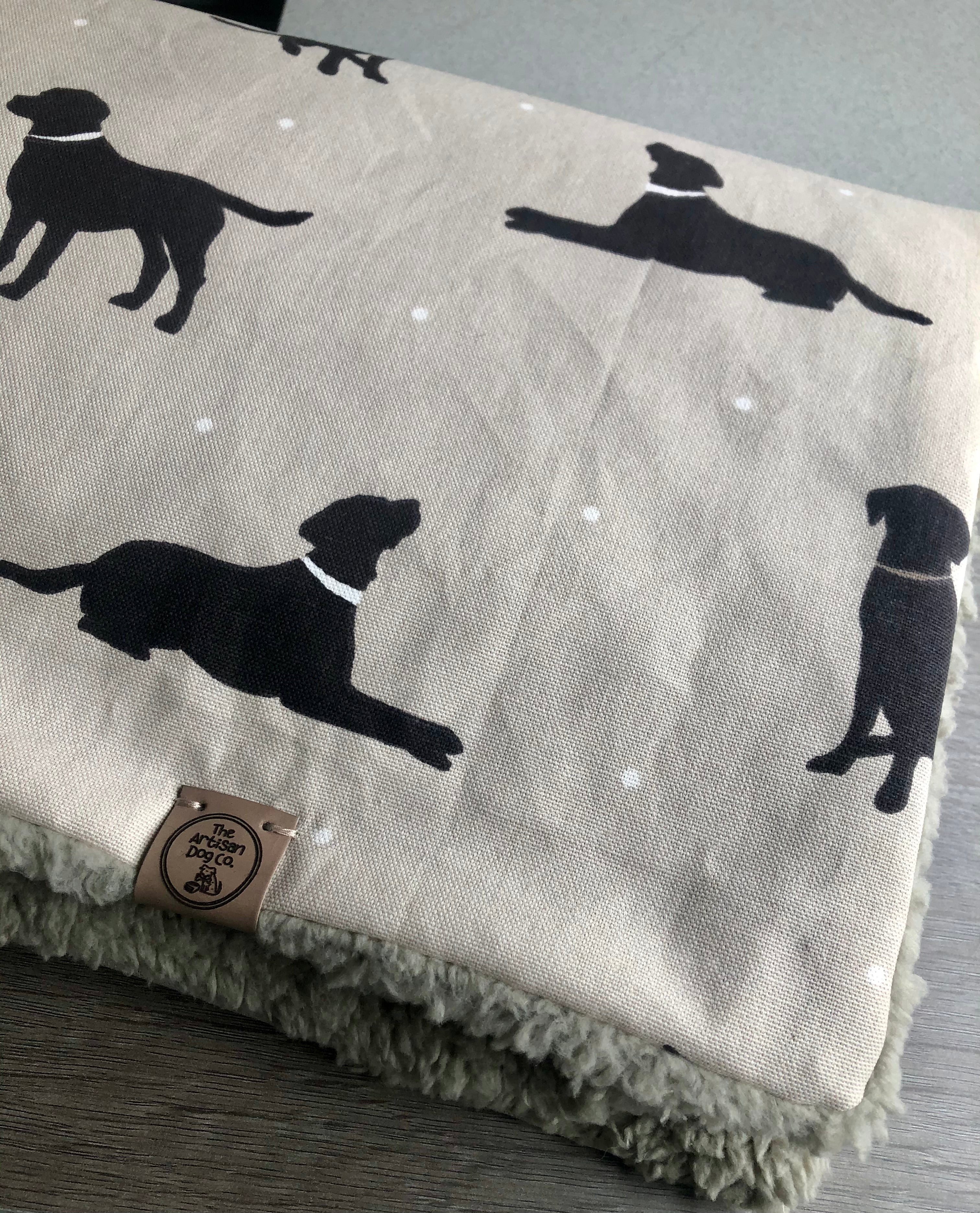 Gray blanket with black dog silhouettes and a brand label on a wooden surface