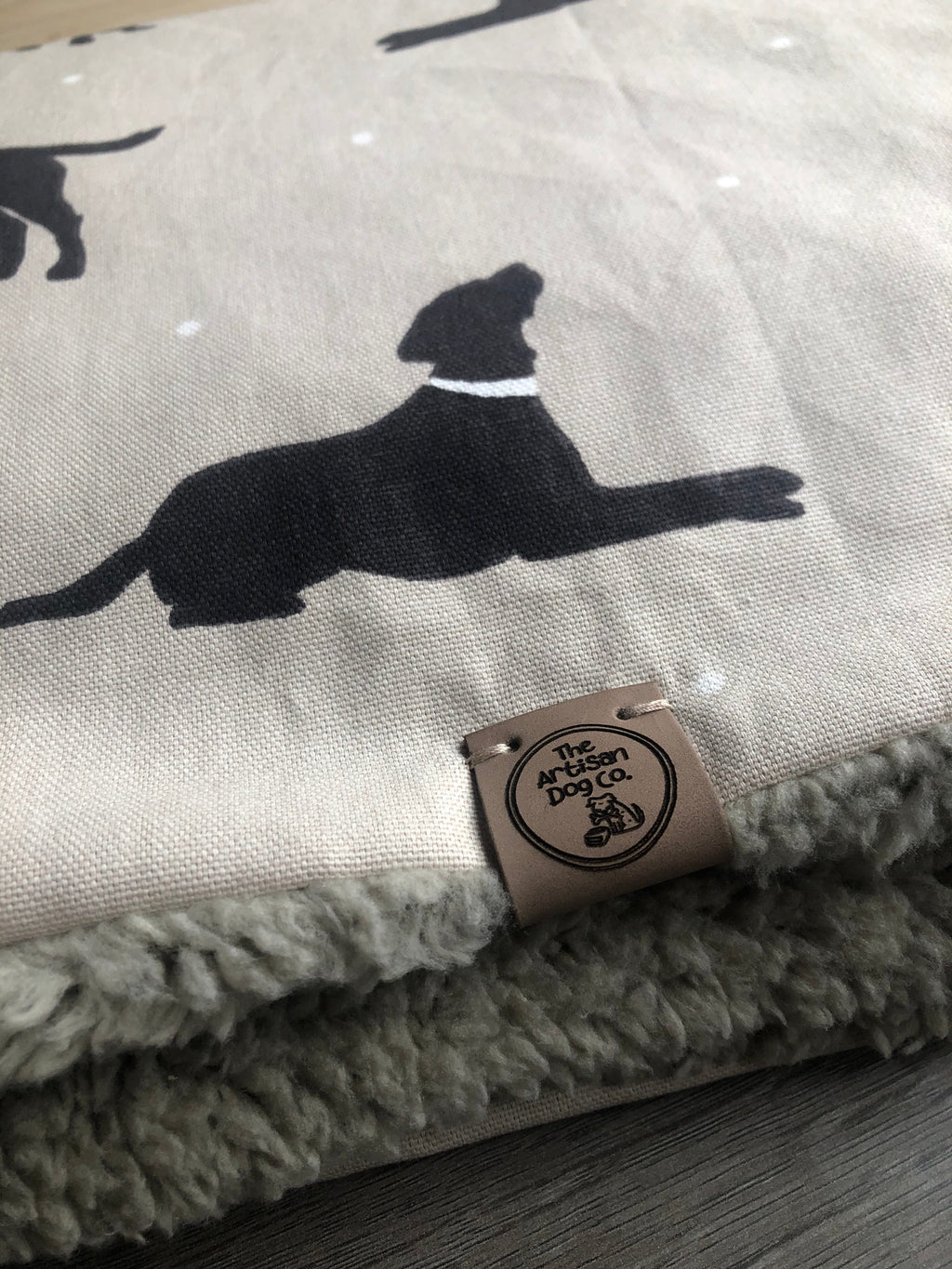 Folded blanket with black dog silhouettes and a brand tag on a wooden surface