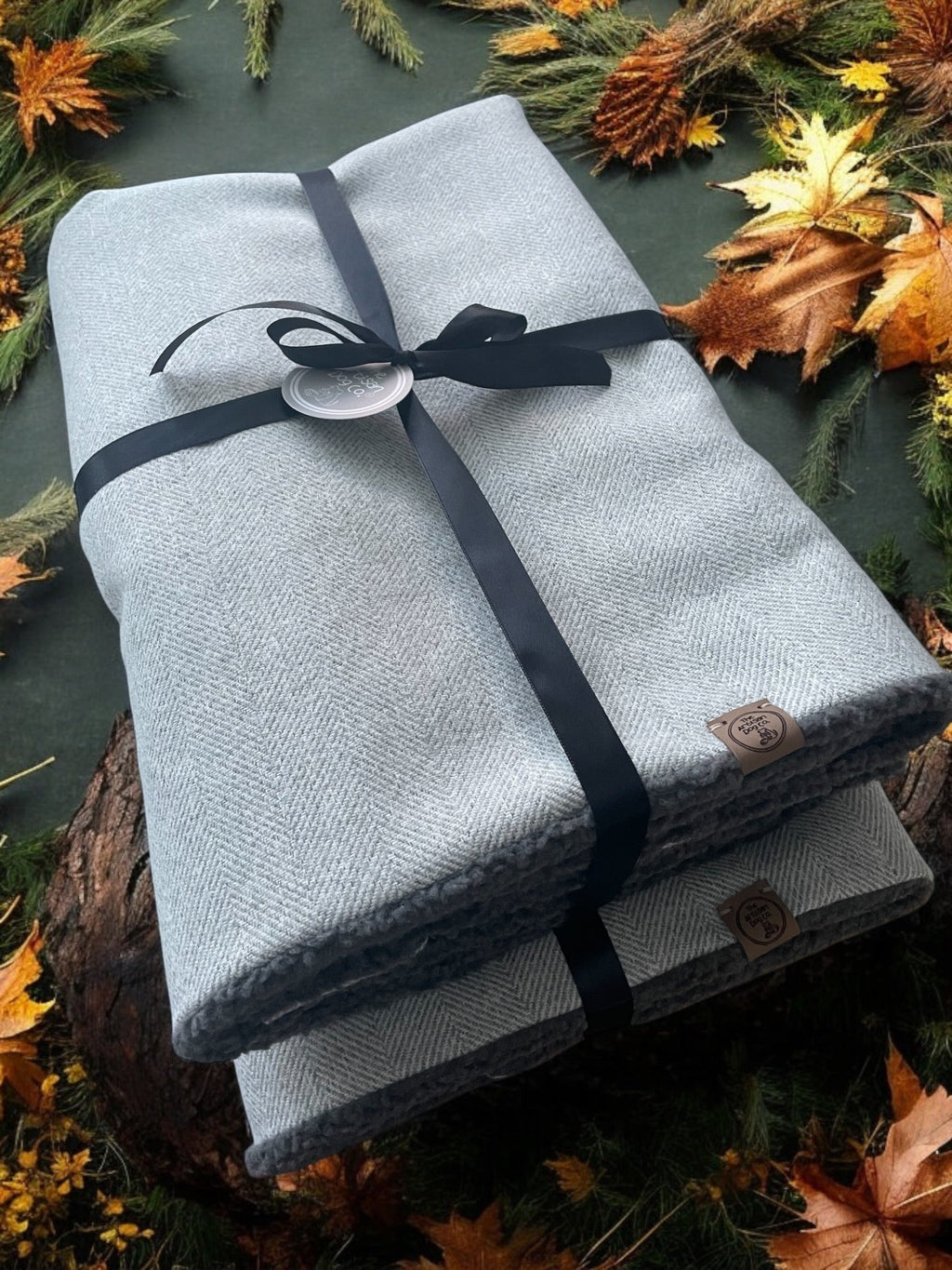 Folded gray blanket with a black ribbon on a surface with autumn leaves