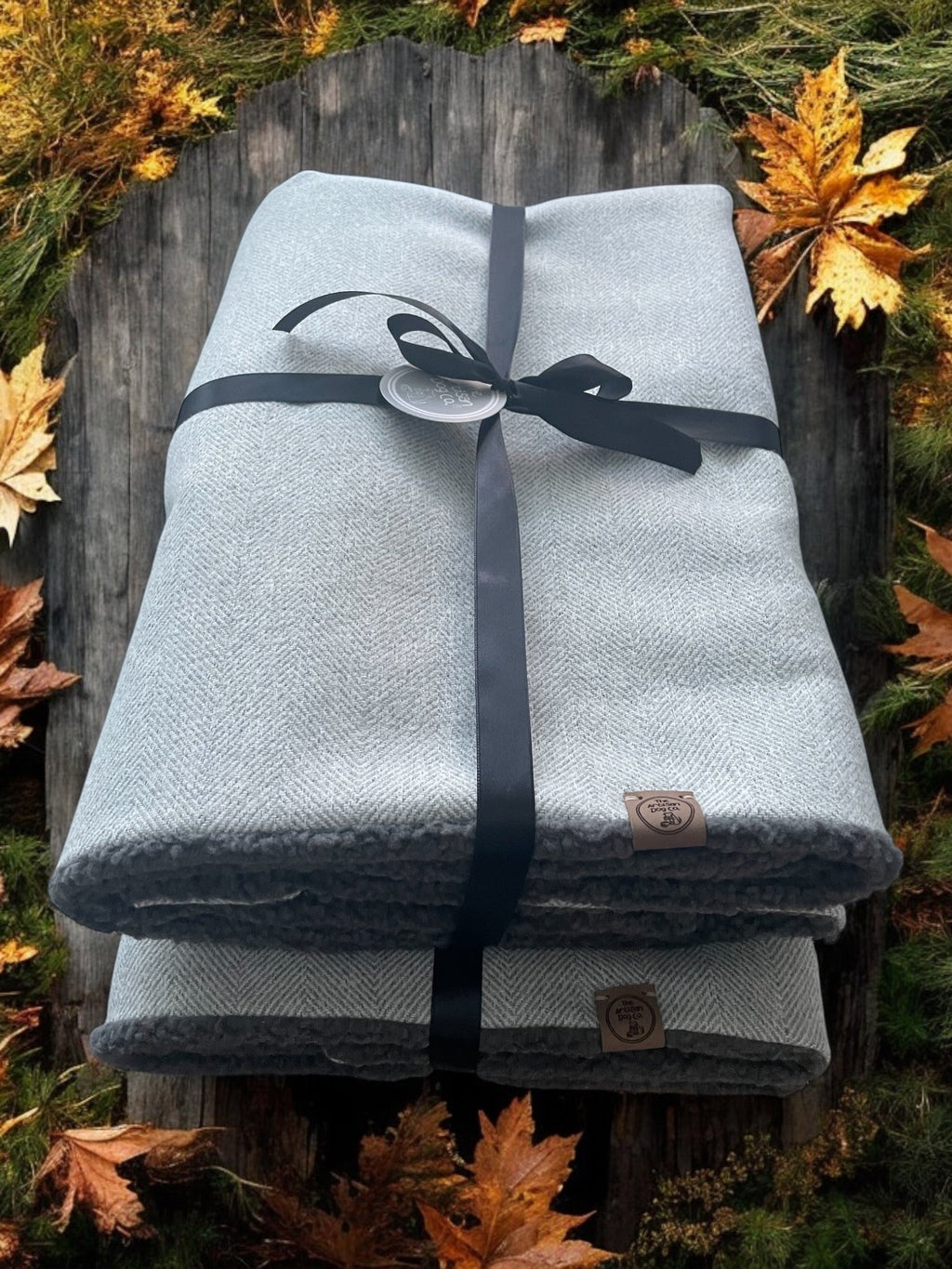 Stack of folded blankets tied with a ribbon on a wooden surface with autumn leaves.