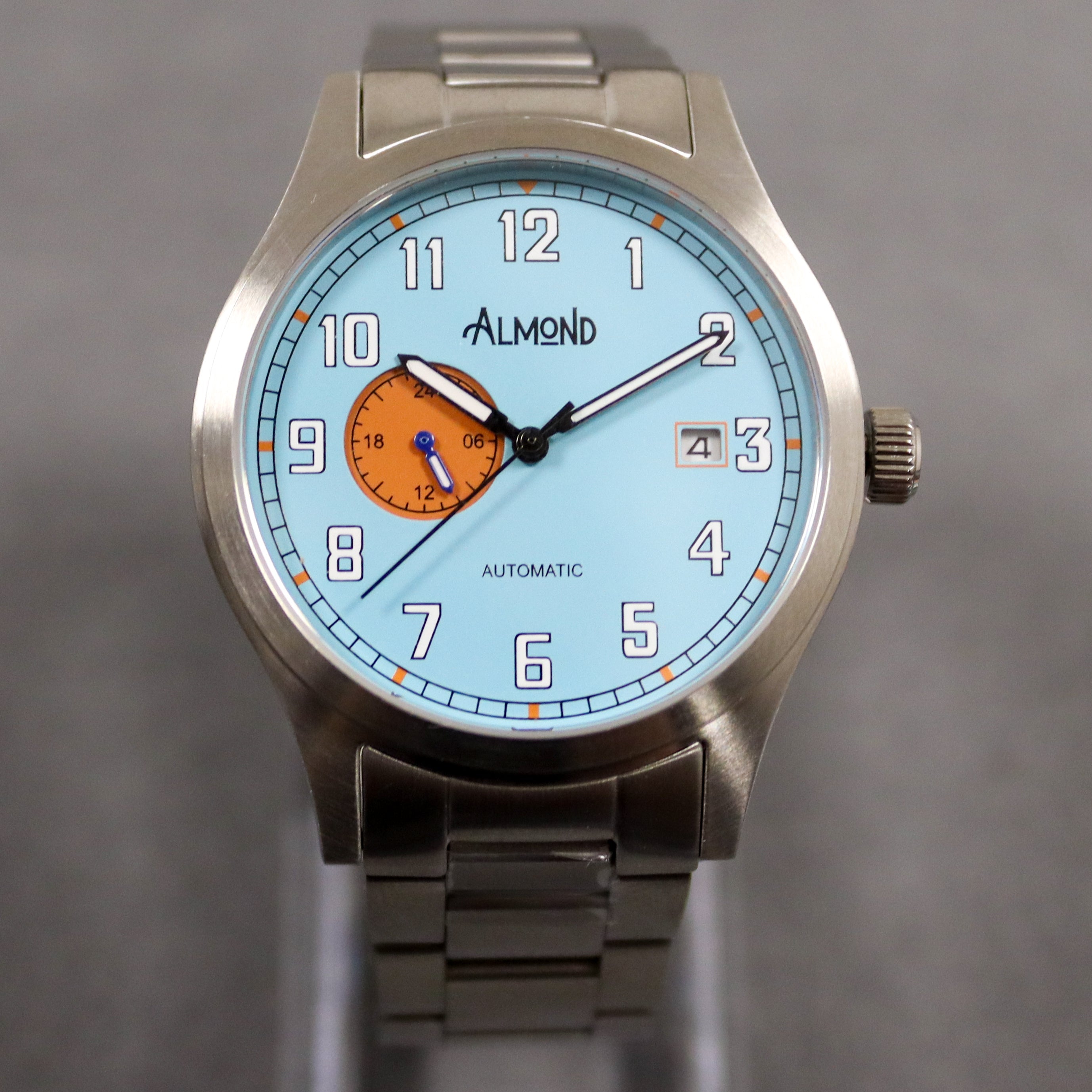 Silver watch with a blue face and orange sub-dial on a gray background