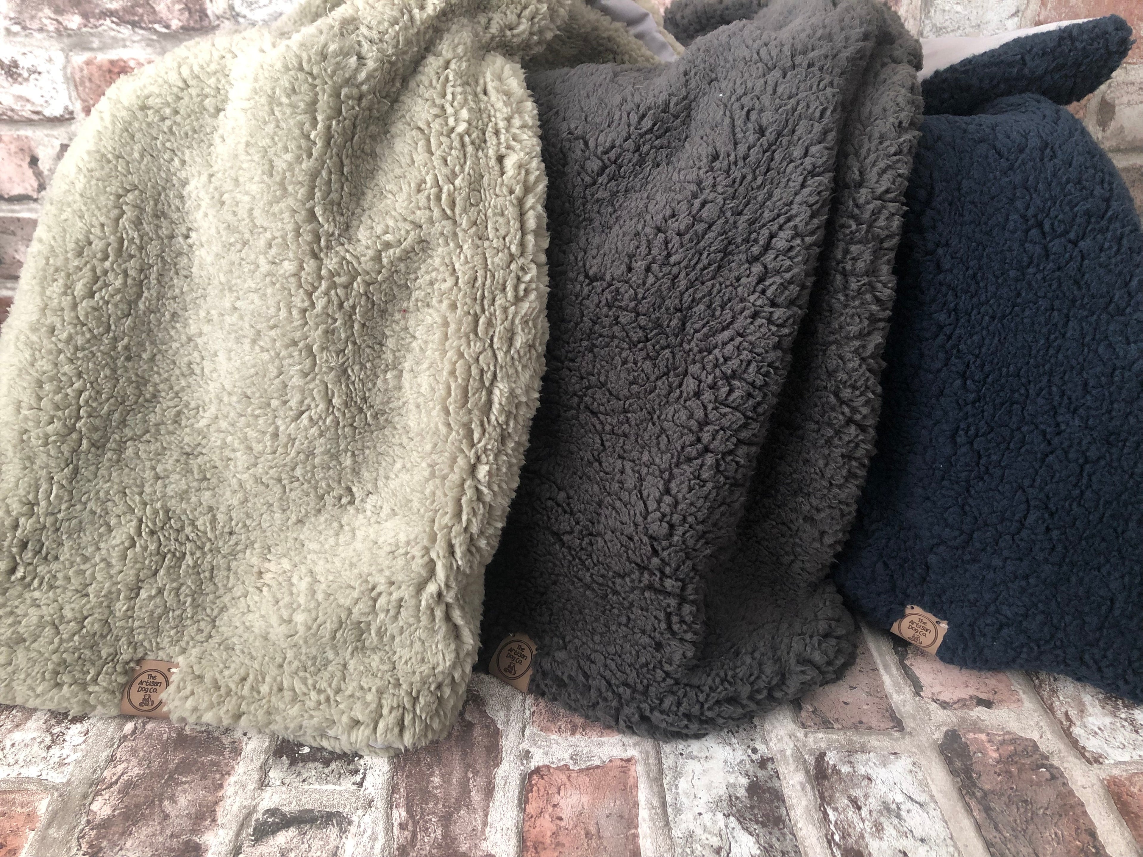Three folded fleece blankets in green, gray, and black on a brick surface.