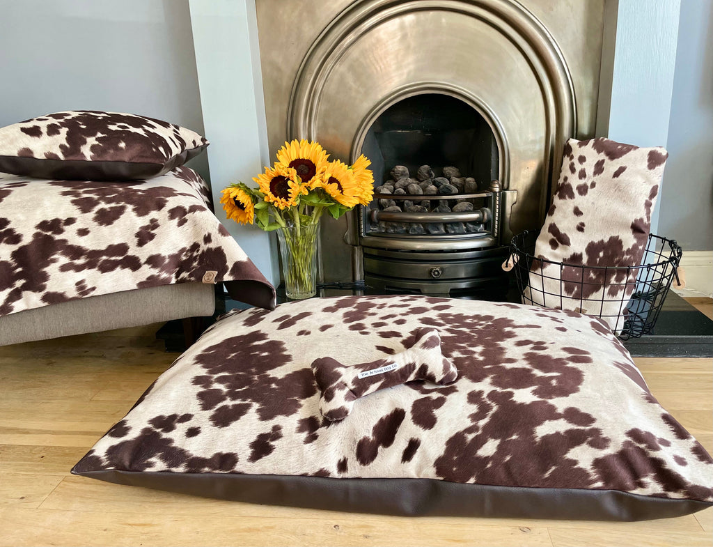 Cow print cushions on a wooden floor with a fireplace and flowers in the background