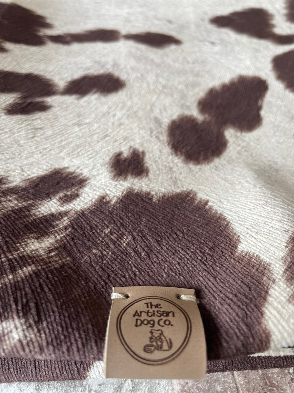 Close-up of a brown and white patterned fabric with a brand tag on a white background