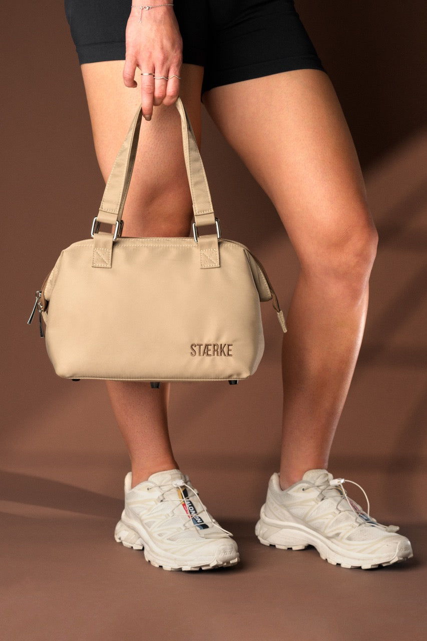 Person holding a beige handbag with 'Stelke' branding on a brown background