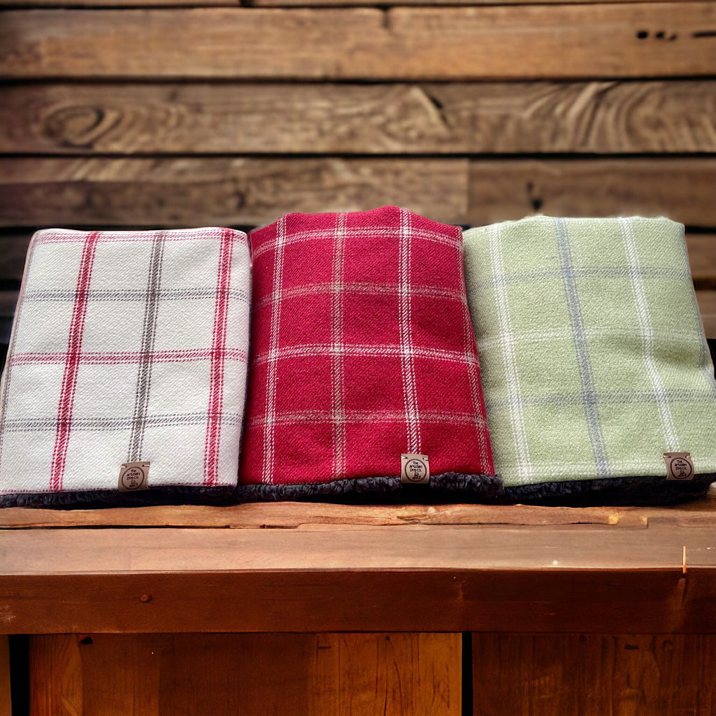Three plaid blankets in white, red, and green on a wooden surface with a wooden background.