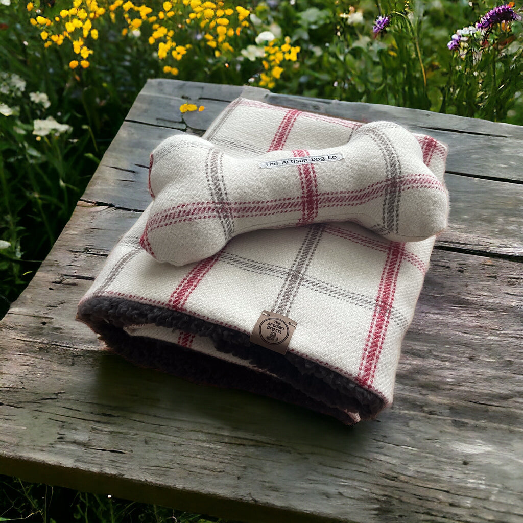 Folded plaid blanket with dog toys on a wooden surface in a garden setting