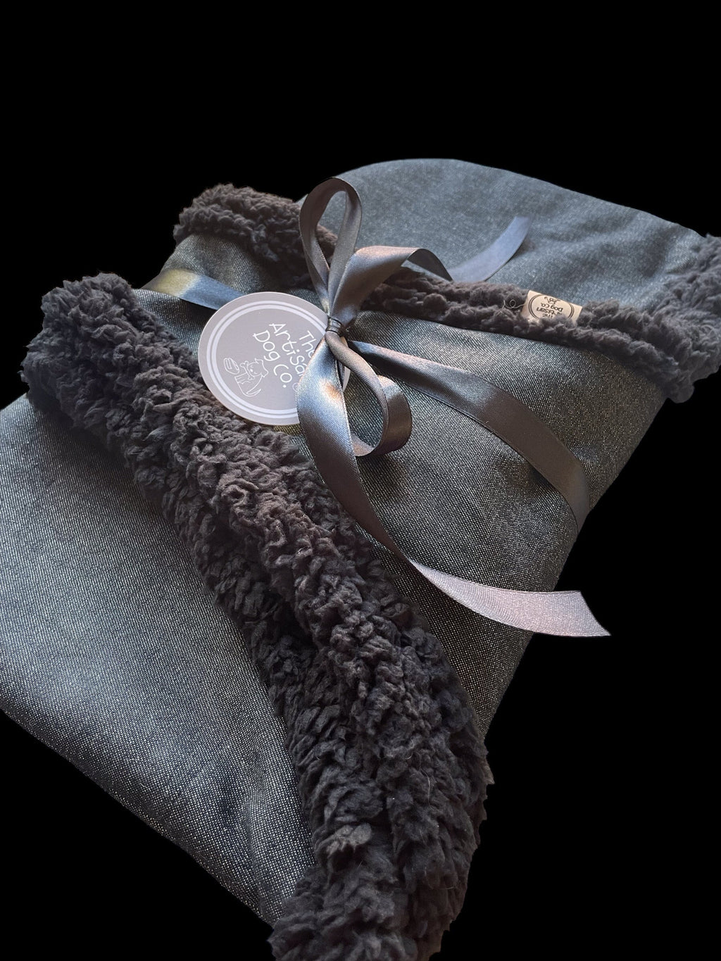 Folded gray blanket with brown fuzzy trim and a ribbon on a black background