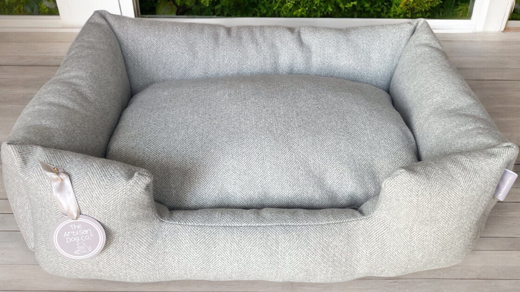 Gray pet bed on a wooden floor with a blurred outdoor background
