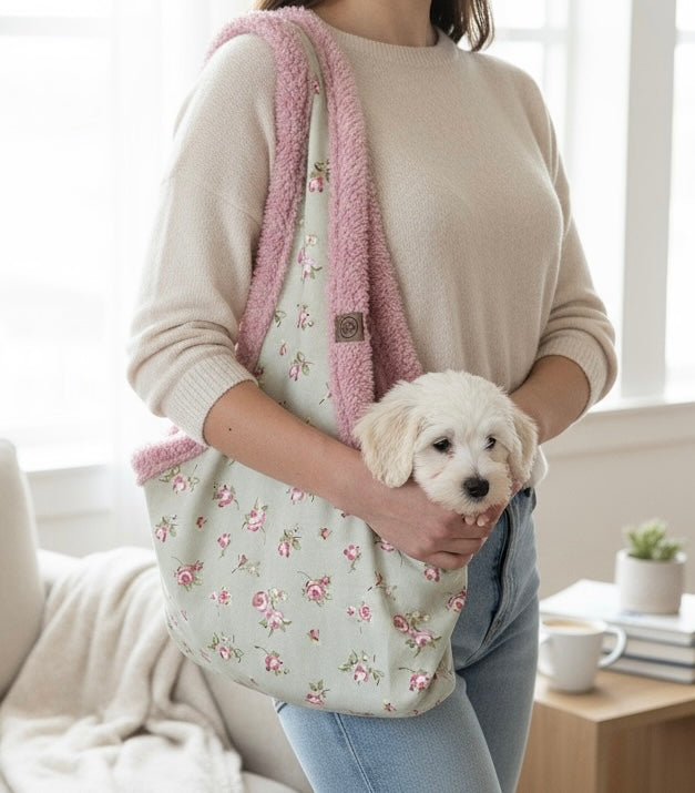 Person holding a small white dog inside a floral-patterned bag with pink trim, in a home setting.