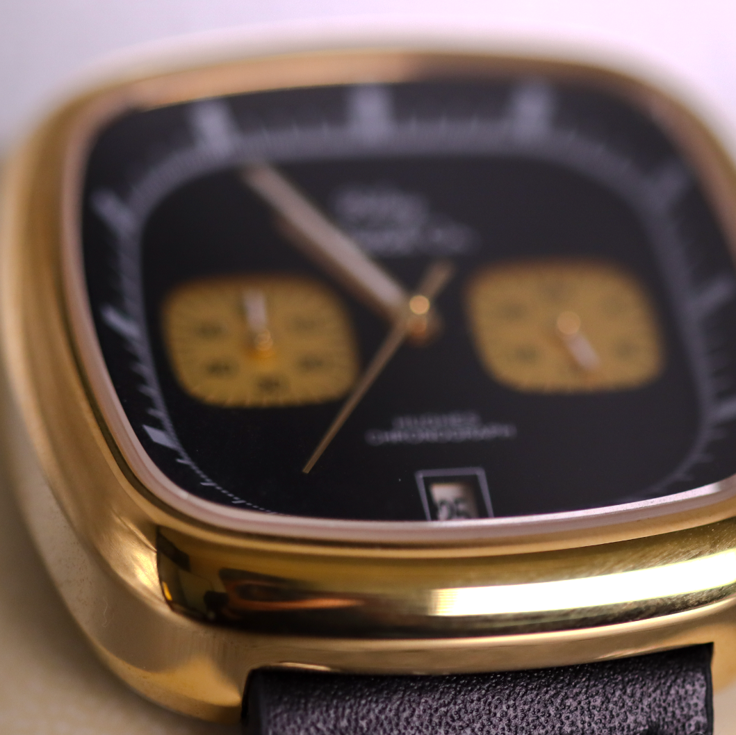 Gold watch with a black face and leather strap on a white background