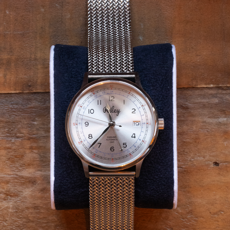 Silver watch with mesh band on a wooden surface