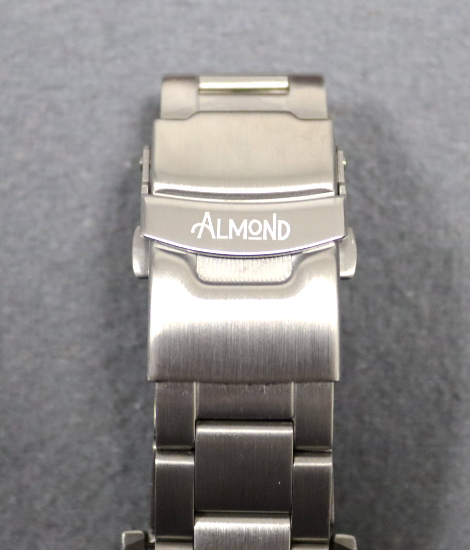 Metallic watch band with 'Almond' branding on a gray background