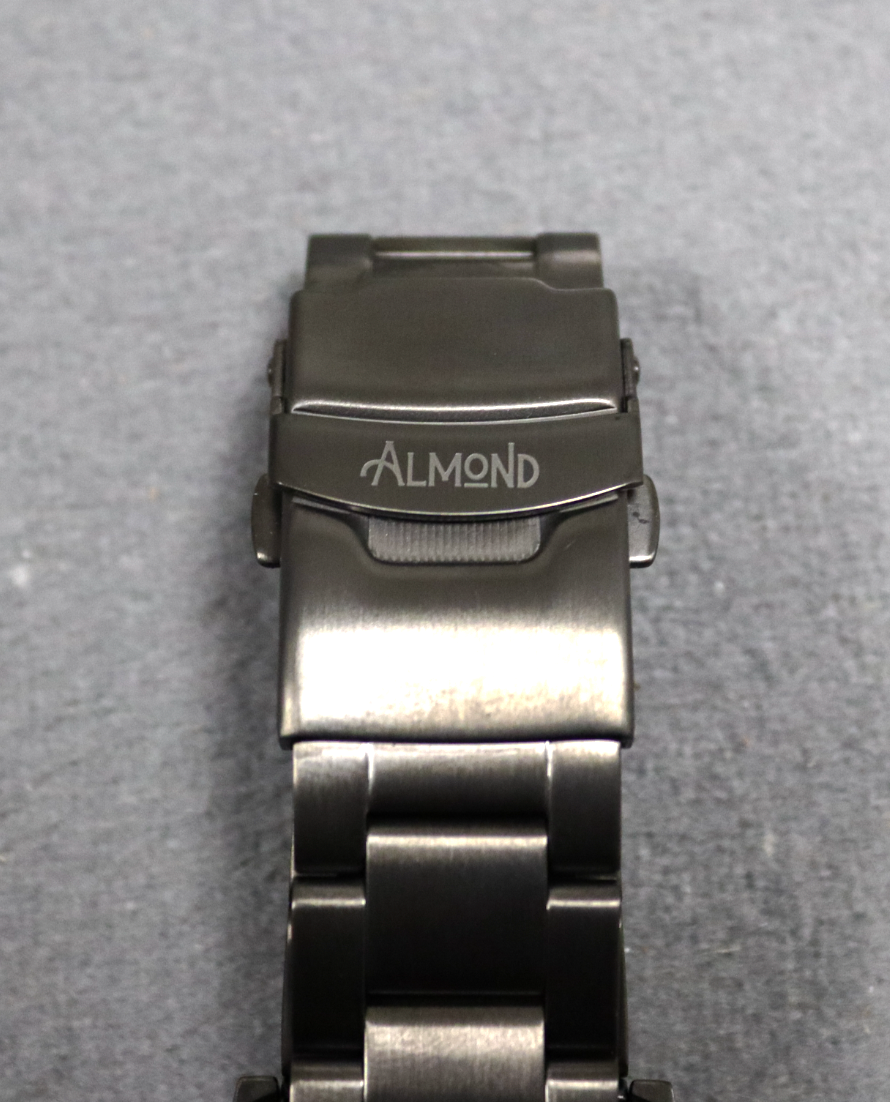 Metallic watch strap with 'Almond' branding on a gray background
