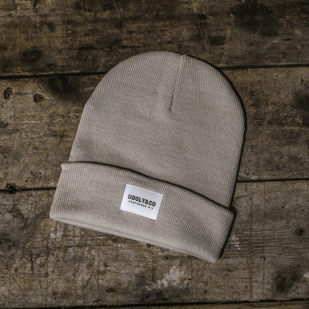 Beige knit beanie with a label on a wooden surface