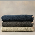 Stack of three folded towels in navy, gray, and beige on a neutral background