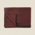 Folded burgundy blanket with black fringe on a beige background