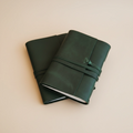 Two green leather journals stacked on a beige background
