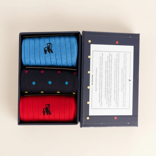 Three pairs of socks in blue, black with colorful dots, and red in a box with a brand logo.
