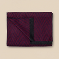 Folded dark red blanket with black edges on a beige background