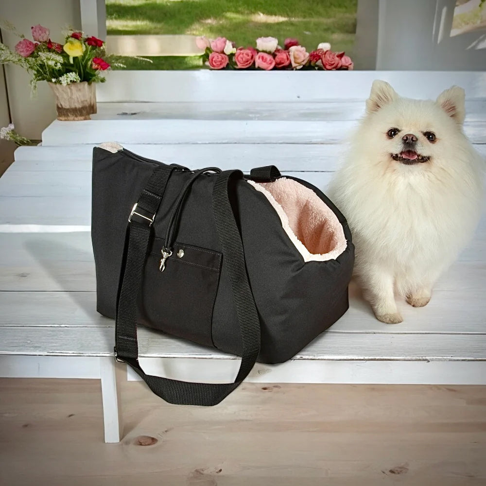 Black pet carrier with a small white dog on a wooden bench, flowers in the background.