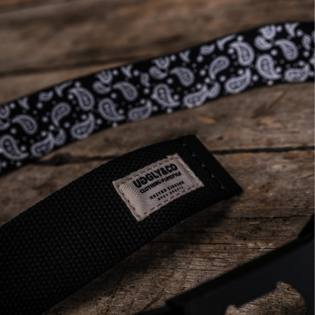 Black belt with white paisley pattern and visible brand label on wooden surface