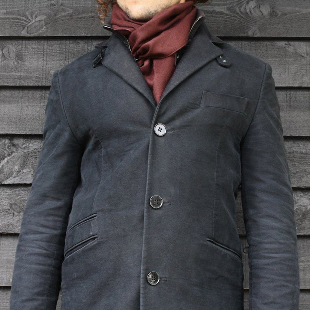 Person wearing a dark gray coat with a red scarf against a wooden wall.