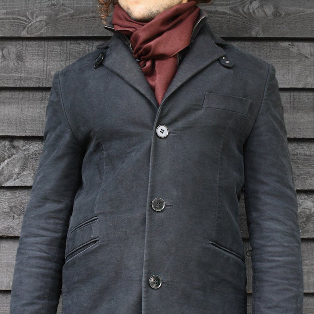 Person wearing a dark gray coat with a red scarf against a wooden wall.