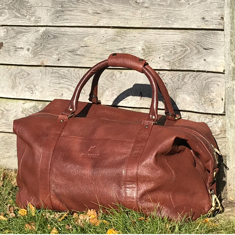 The Boston. A classic brown leather holdall by Burghley Bags. Handmade from finest, hardwearing grained leather. Features metal feet and comes with a shoulder strap.  Meets most airline carry-on requirements.