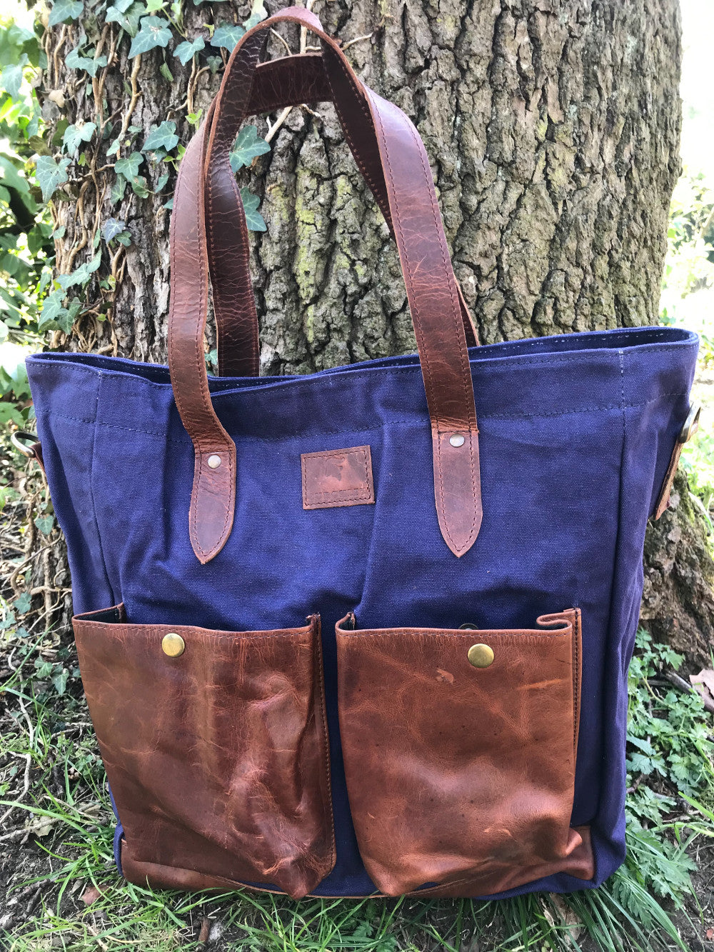 The Bingham.  A large zipped tote bag by Burghley Bags.  Handmade from eco-friendly vegetable tanned leather and strong cotton canvas, with a canvas shoulder strap. Shown in modern blue.